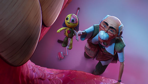 An elderly man with white hair and glasses holds a small yellow rag doll toward a large, pink, open mouth.
