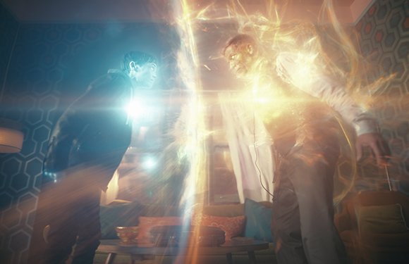 Two men stand on opposite sides of a glowing, golden energy rift in a room.