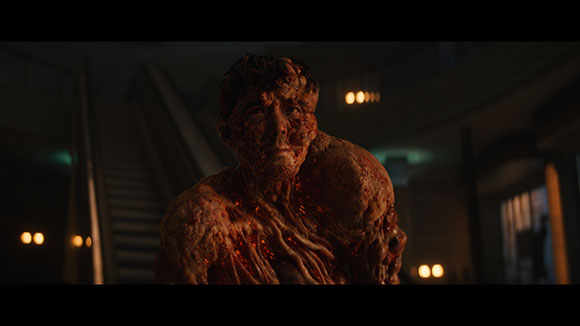 A muscular humanoid figure with dark, textured, and glowing orange skin in a dimly lit room.