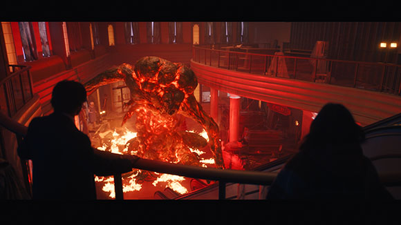 A giant creature made of molten lava and rock stands amidst flames in a large, dimly lit hall.
