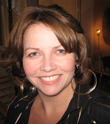 A smiling woman with shoulder-length brown hair and large silver hoop earrings.