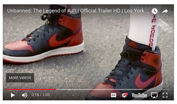 Close-up of black and red high-top sneakers worn with white socks on a paved surface.