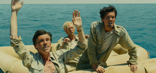 Three men in tan clothing sit in an inflatable life raft on a vast blue ocean with arms raised.