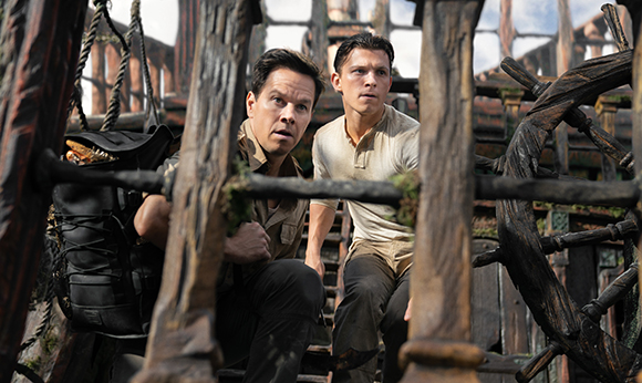 Two men crouch behind weathered wooden beams in a ruined structure.