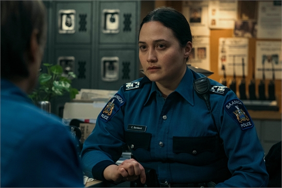 A female police officer in a blue uniform looks intently at someone off-camera.