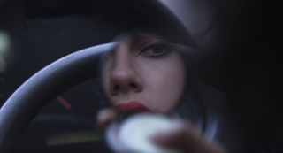 Reflection of a person's eyes, nose, and lips in a car's rearview mirror in low light.