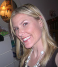 A smiling blonde woman with long hair wearing a white beaded necklace.