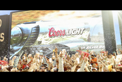 A crowd of people with their hands raised in front of a large Coors Light billboard.