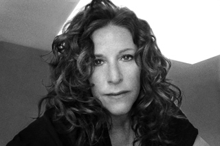 Black and white close-up portrait of a woman with long, voluminous curly hair looking toward the camera.