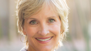 A smiling woman with short blonde hair and green eyes wearing hoop earrings.