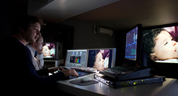 Editors working in a dark room with several glowing computer monitors displaying video content.