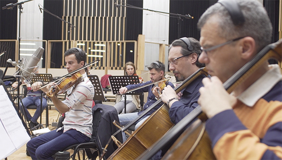 Orchestra musicians playing string instruments in a recording studio with microphones.