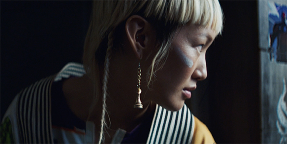 Profile of a person with blonde hair, a single earring, and a light mark on their cheek.
