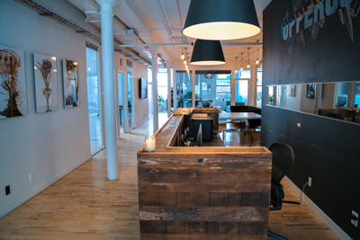 A modern office space with light wood floors, wooden partitions, and large black pendant lamps.
