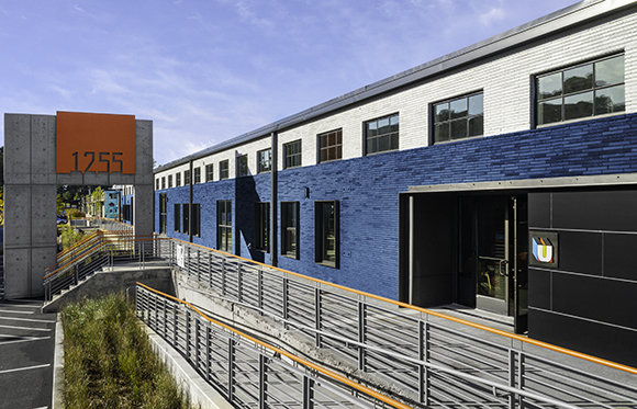 A modern two-story building with a blue brick lower half and white brick upper half under a blue sky.