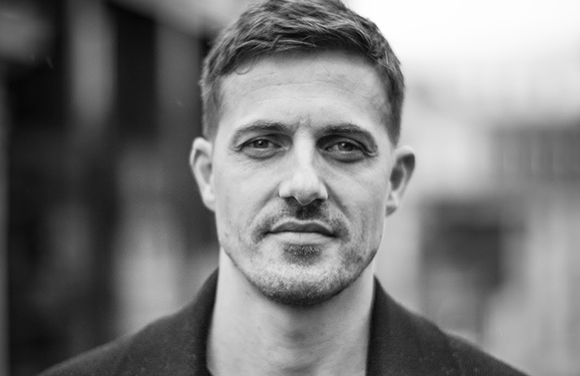 Black and white close-up portrait of a man with short hair and light facial stubble.