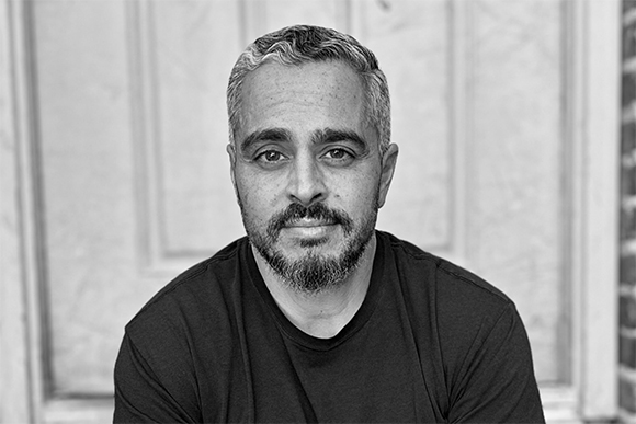 Black and white headshot of a man with short salt-and-pepper hair and a beard wearing a dark t-shirt.
