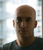 Close-up portrait of a bald man with a serious expression looking directly at the camera.
