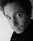 Black and white close-up portrait of a man looking slightly upward with a neutral expression.