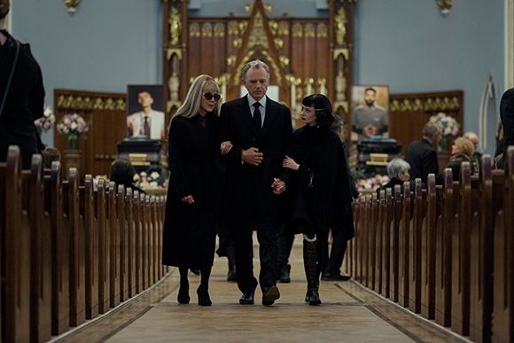Three people dressed in black walk down the center aisle of a church toward the camera.