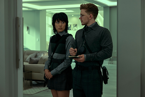 A man with glasses and a woman with dark hair stand in a doorway, looking to the side in a modern interior.