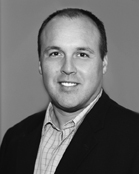 Black and white portrait of a smiling man wearing a dark blazer and a light-colored button-down shirt.