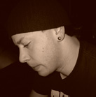 Side profile of a person wearing a dark beanie and a small stud earring, looking down.