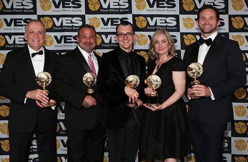 Five people in formal wear stand in a row holding gold trophies against a VES backdrop.