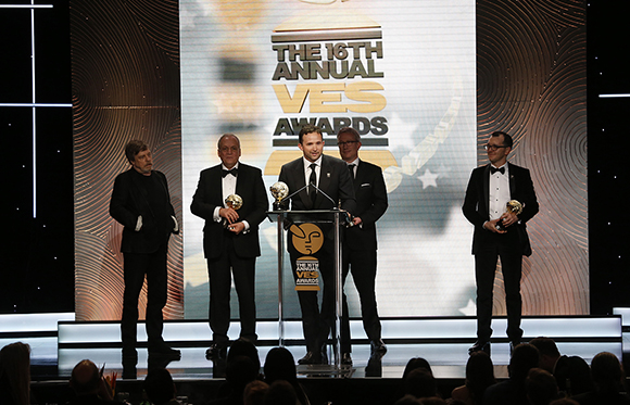 Five men in black tie attire stand on a stage in front of a large screen reading The 16th Annual VES Awards.