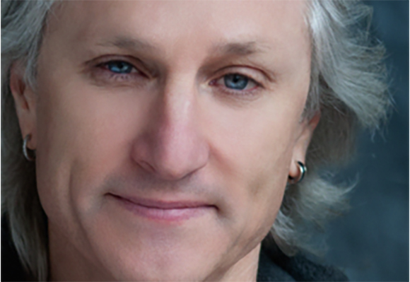 Close-up portrait of a man with light hair, blue eyes, and small hoop earrings.