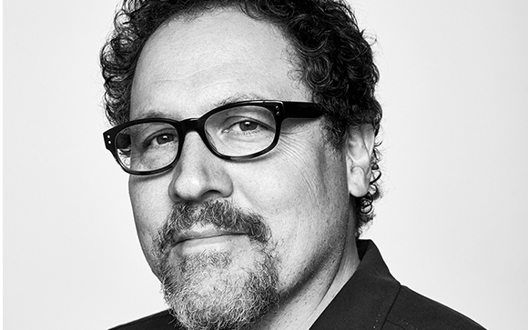 Black and white close-up portrait of a man with curly hair, glasses, and a goatee looking at the camera.