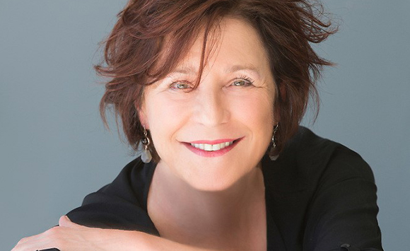 A smiling woman with short reddish-brown hair and silver earrings against a gray background.