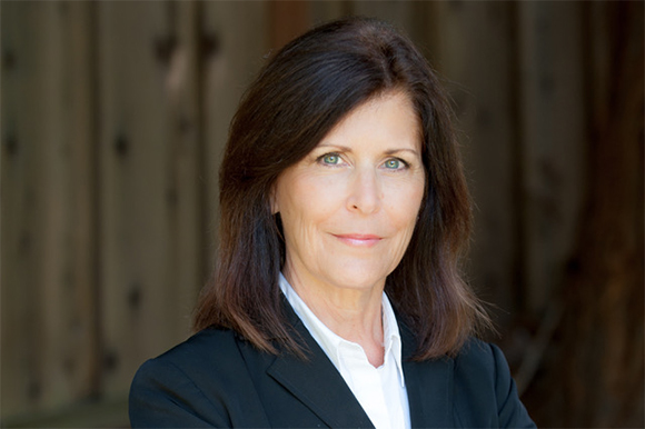 A woman with shoulder-length brown hair wearing a white shirt and black blazer, smiling slightly.