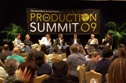 Panelists sit on a stage in front of a banner for The Production Summit '09, with an audience in the foreground.