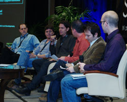 Six men sit in a row of chairs on a stage during a panel discussion.