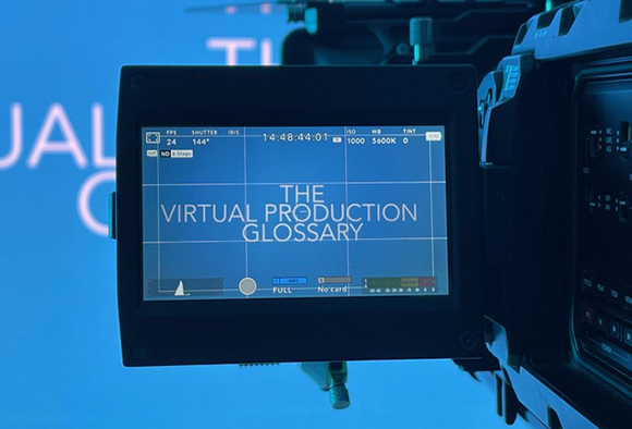 A close-up of a professional camera monitor displaying the text 'THE VIRTUAL PRODUCTION GLOSSARY' over a blue screen.