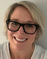 A smiling woman with short blonde hair and black-rimmed glasses wearing a white shirt.