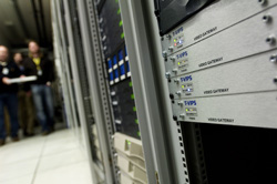 Close-up of stacked video gateway server units in a data center with blurred people in the background.