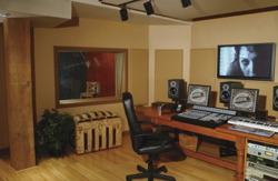 A recording studio control room with a wooden desk, computer monitors, studio monitors, and a black office chair.