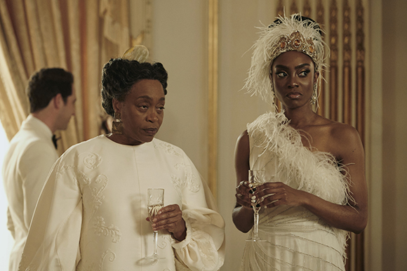 Two women in elegant white formal wear holding champagne glasses in a luxurious room.