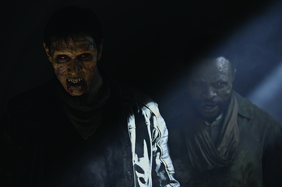 Two pale, monstrous figures with glowing eyes and bloodied mouths emerge from the darkness.