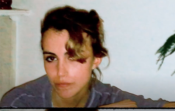 A close-up portrait of a person with wavy hair looking toward the camera.