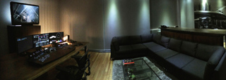 A dark room featuring a desk with multiple monitors and a large L-shaped sectional sofa.