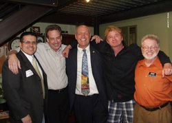 Five men standing in a row, smiling with their arms around each other's shoulders.