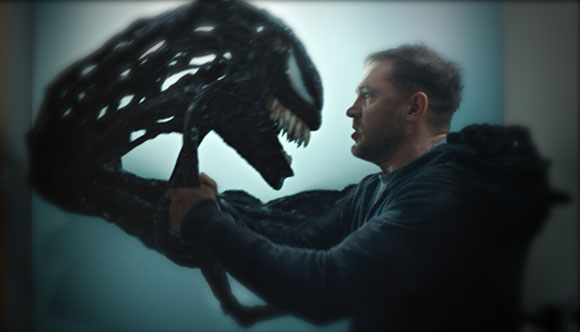 A man stares intensely at a large, black, toothy creature with a long, textured head.