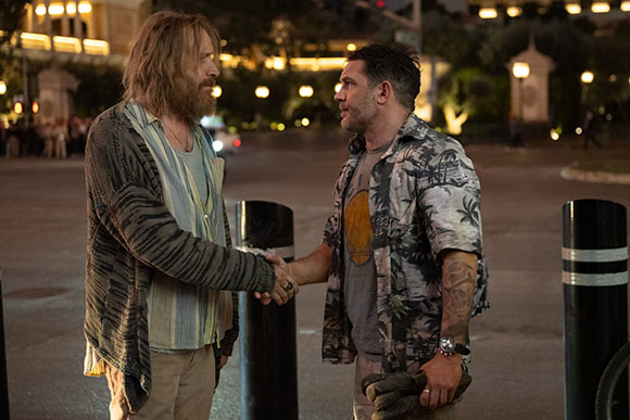 Two men stand on a street at night, shaking hands.