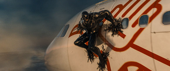 A black, oily creature with tendrils clings to the exterior of a white airplane in flight.