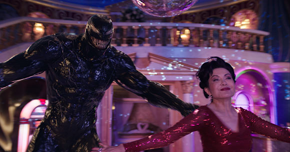 A large black creature with sharp teeth stands behind a woman in a sparkling red dress in a lit ballroom.