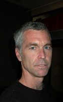 A man with short gray hair and blue eyes wearing a black shirt.