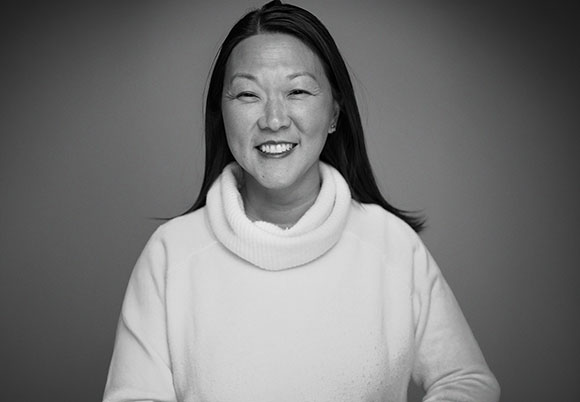 Black and white portrait of a smiling woman with long dark hair wearing a white turtleneck sweater.